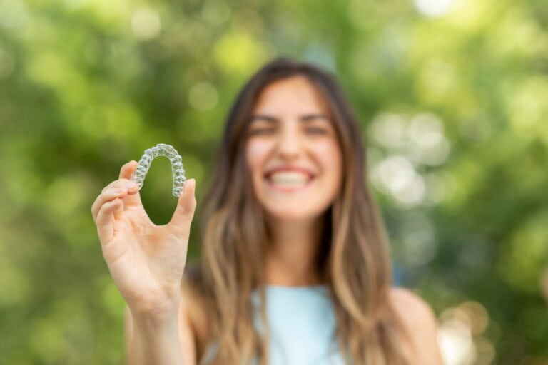 A lady holds up his Invisalign retainer, showing off how inconspicuous it is.