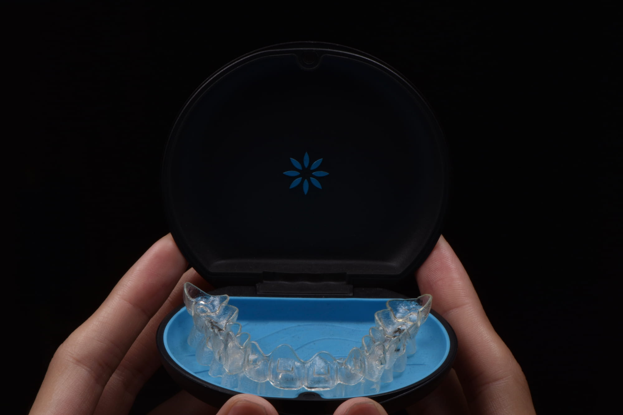 A person holds up an Invisalign retainer in its case.